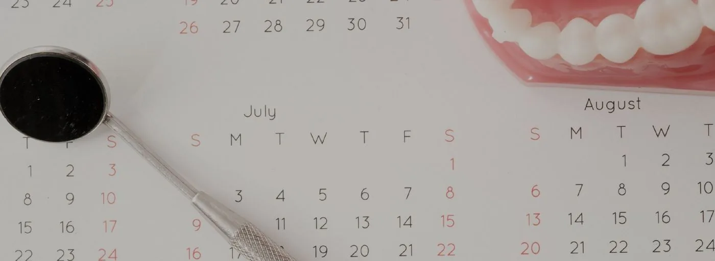 Dental mirror resting on an appointment calendar beside a denture model